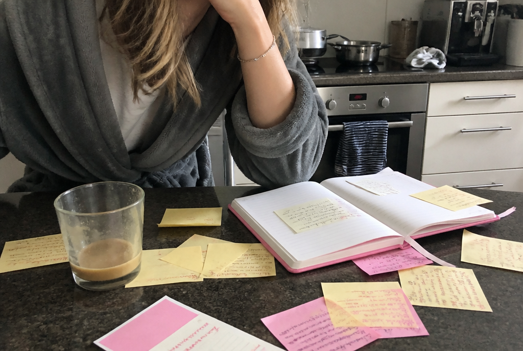 A hand at the forehead beside a worktop covered in reminder notes